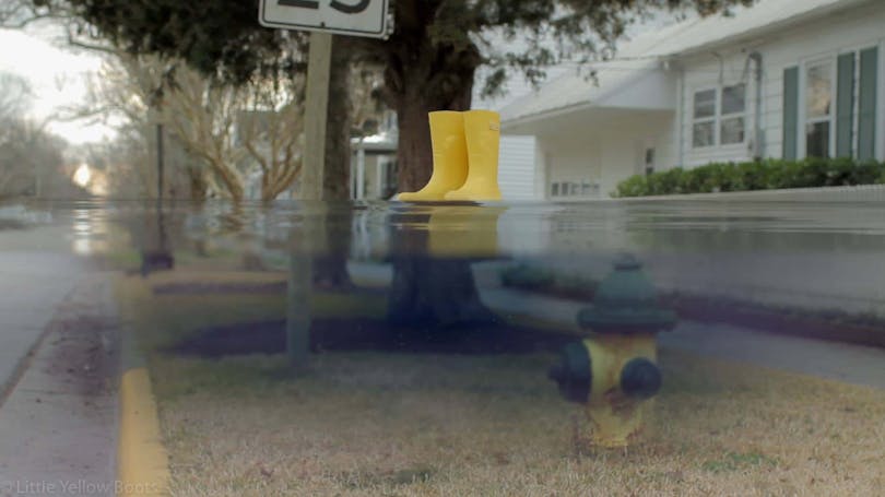 Ett par gula stövlar svävar ovanpå en vattenyta framför ett hus i USA.