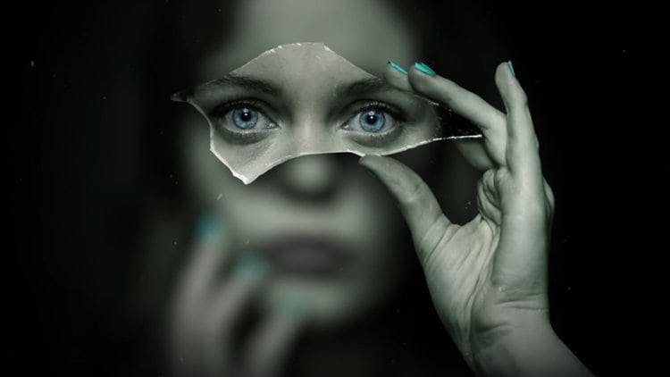 En kvinna håller upp en glasbit framför sitt ansikte och hennes ögon syns tydligt, allt annat är suddigt.