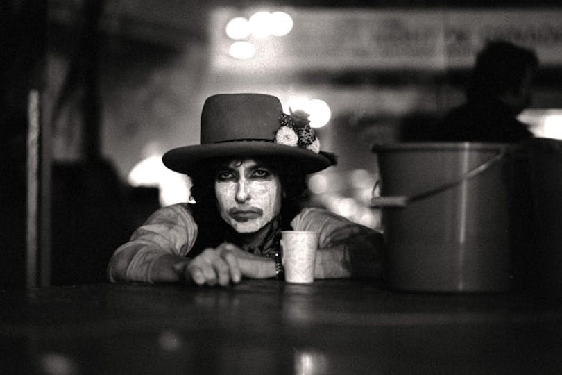 Bob Dylan är vitmålad i ansiktet på en bar, medan han kollar rakt in i kameran.